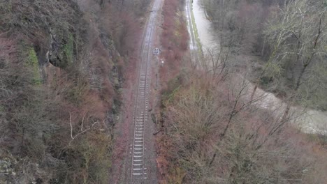 Empty-Train-Track-Surrounded-With-Deciduous-Trees-Next-To-River-With-Strong-Current