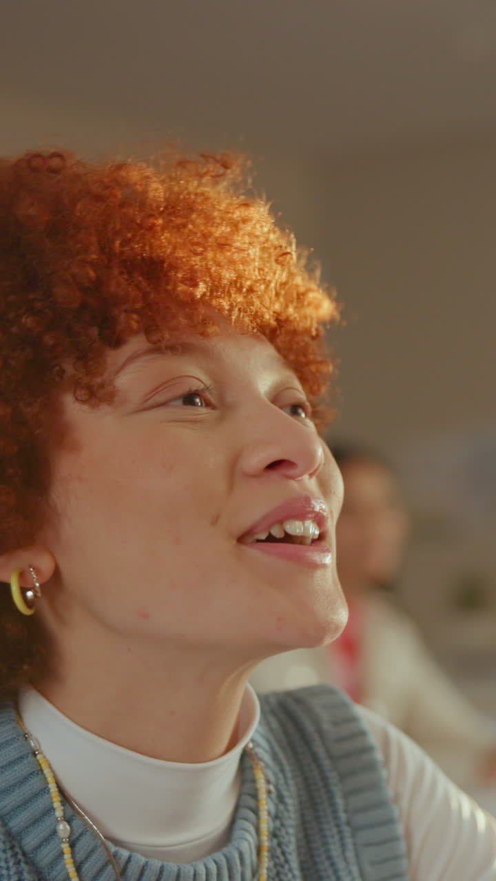 Primo piano di giovane donna con capelli rossi ricci che sorride in classe.