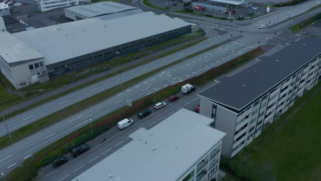 Toma-En-ángulo-Alto-De-Poco-Tráfico-En-Una-Carretera-De-Varios-Carriles-Entre-Edificios-De-Apartamentos-De-Varios-Pisos-Y-Un-Sitio-Industrial-O-Logístico.-Reikiavik,-Islandia