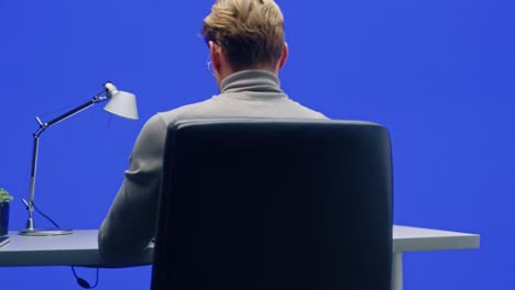office green screen background: businessman sitting at his desk working on a laptop computer. man working with big data e-commerce analysis. 360 degree chroma key tracking shot. camera moving around