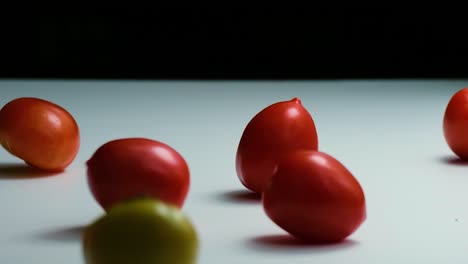 reversed slow motion shot of tomatoes of different colours falling, bouncing and rolling onto a white surface untill they stop moving