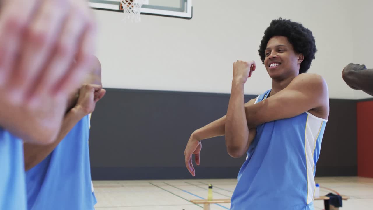 Happy diverse male basketball players stretching arms and talking at training session, slow motion