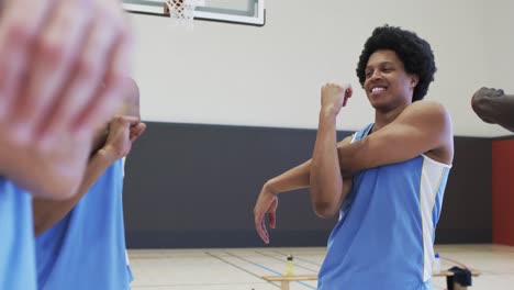 happy diverse male basketball players stretching arms and talking at training session, slow motion