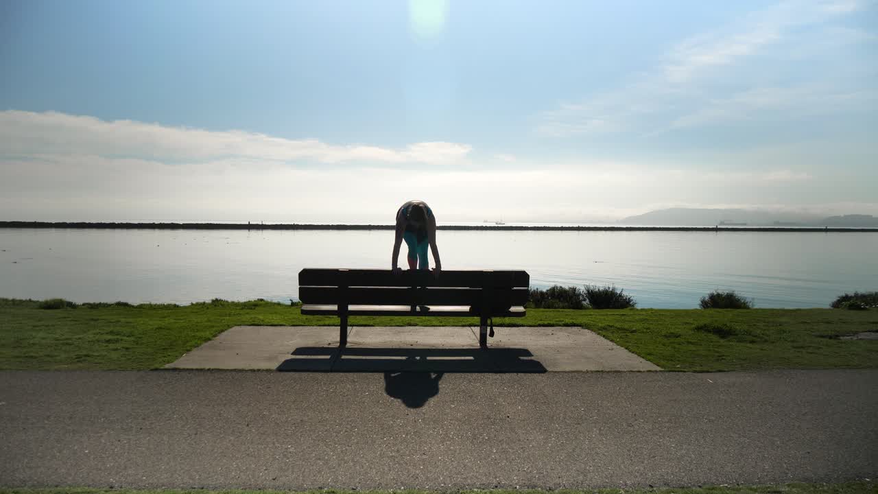 Young athletic girl does a handstand, split and dismount on park bench