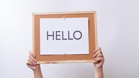 woman's hand shows the paper on board with the word hello in white studio background with copy space