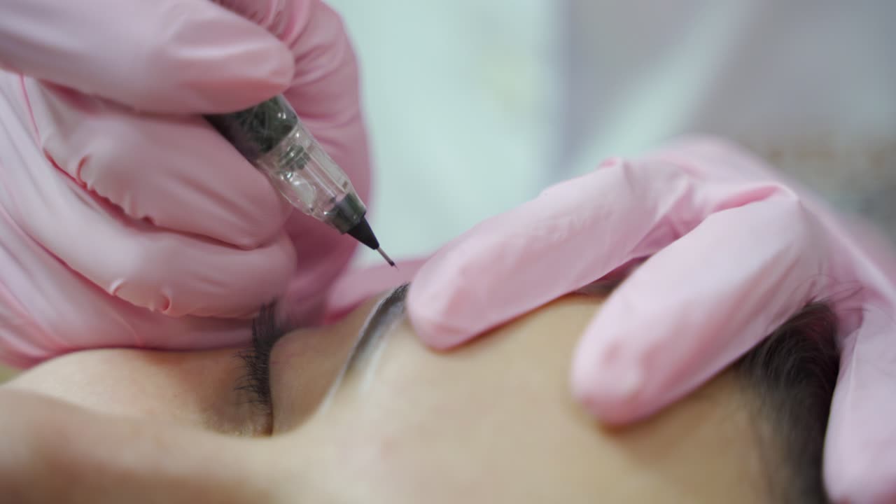 beautician in gloves is drawing the shape of the eyebrows with a special needle. The procedure of permanent makeup of eyebrows