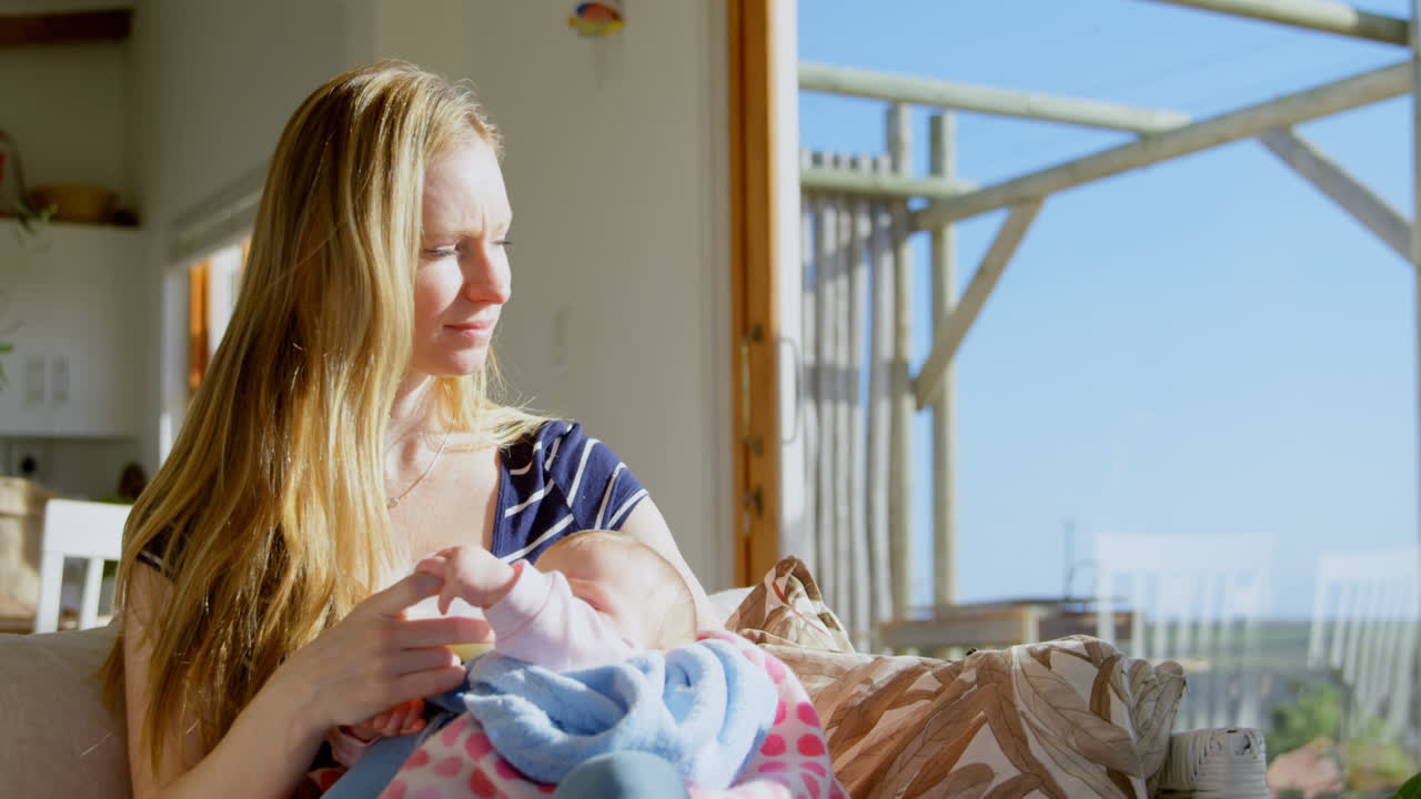 Vue de face d'une mère caucasienne d'âge moyen donnant le biberon à son bébé dans une maison confortable 4k