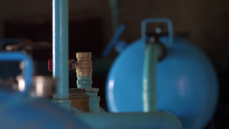 close up view of piping inside water pump room with blurred background of blue tank