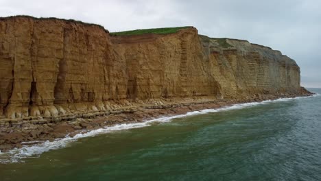 static drone shot of a famous jurassic coast beach cliff face in dorset. captured on a cloudy day shows gentle waves landing up on the sand.