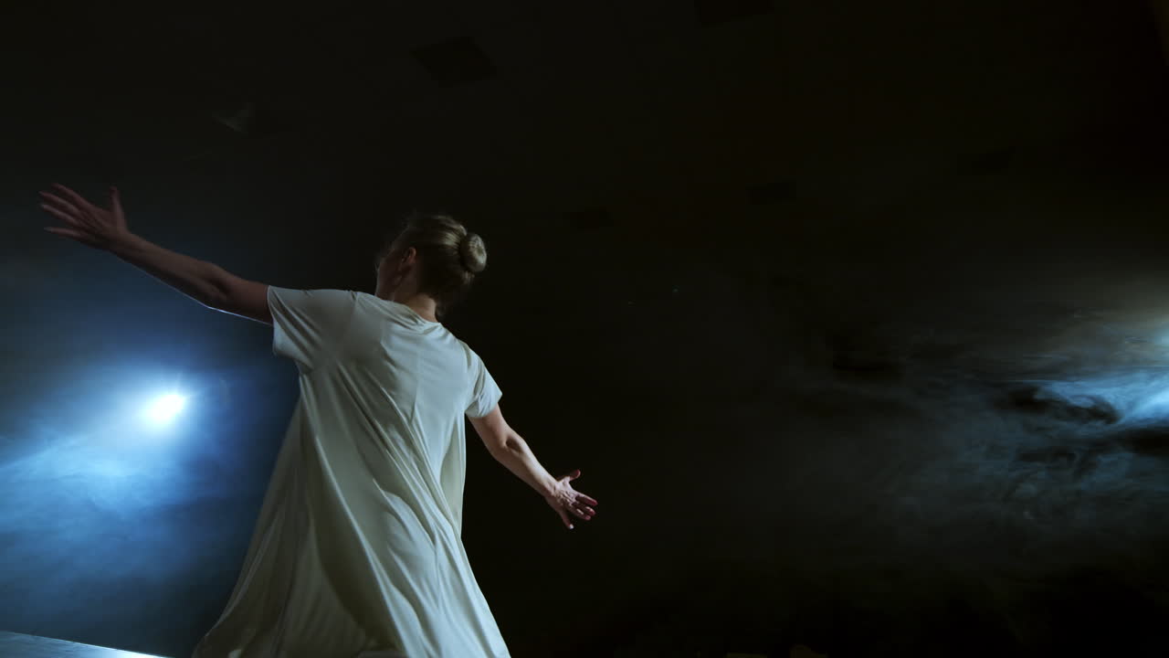 giros dramáticos y saltos de una bailarina de ballet moderna de un musical. una mujer soltera baila emocionalmente en el escenario contra un fondo oscuro con humo en el centro de atención en cámara lenta.