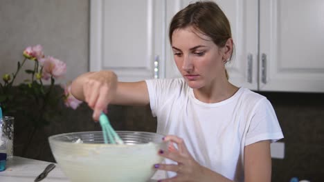 Una-Mujer-Joven-Prepara-Masa-Mezclando-Ingredientes-En-El-Recipiente-Usando-Un-Batidor-En-La-Cocina.-Comida-Hecha-En-Casa.-Tiro-En-Cámara-Lenta