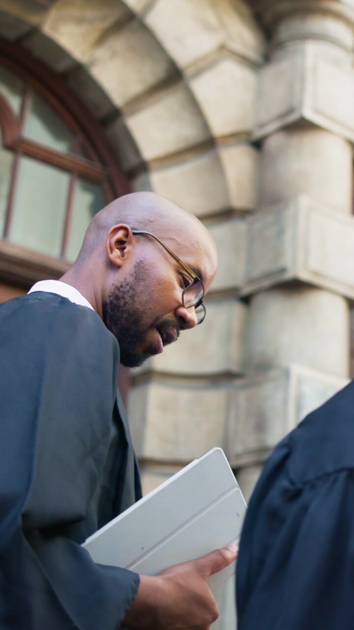 Lawyer in Academic Robe Holding Tablet Outside Courthouse