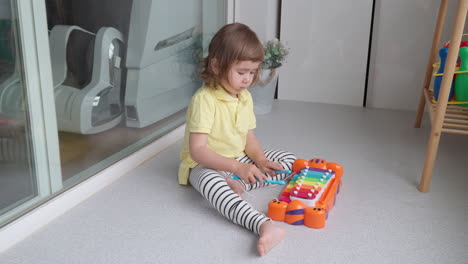 mixed ethnicity toddler of asian descent sitting on floor playing with toy xylophone at home balcony