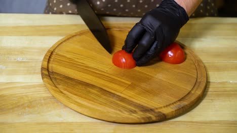 vista de cerca de las manos del chef en guantes cortando tomate en rebanadas en una tabla de corte de madera redonda