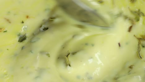 macro shot of spoon mixing homemade white sauce, mayo, seasoned with parsley