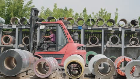 forklift driver loads rolls of steel sheet. industrial warehouse with rolls of steel sheet