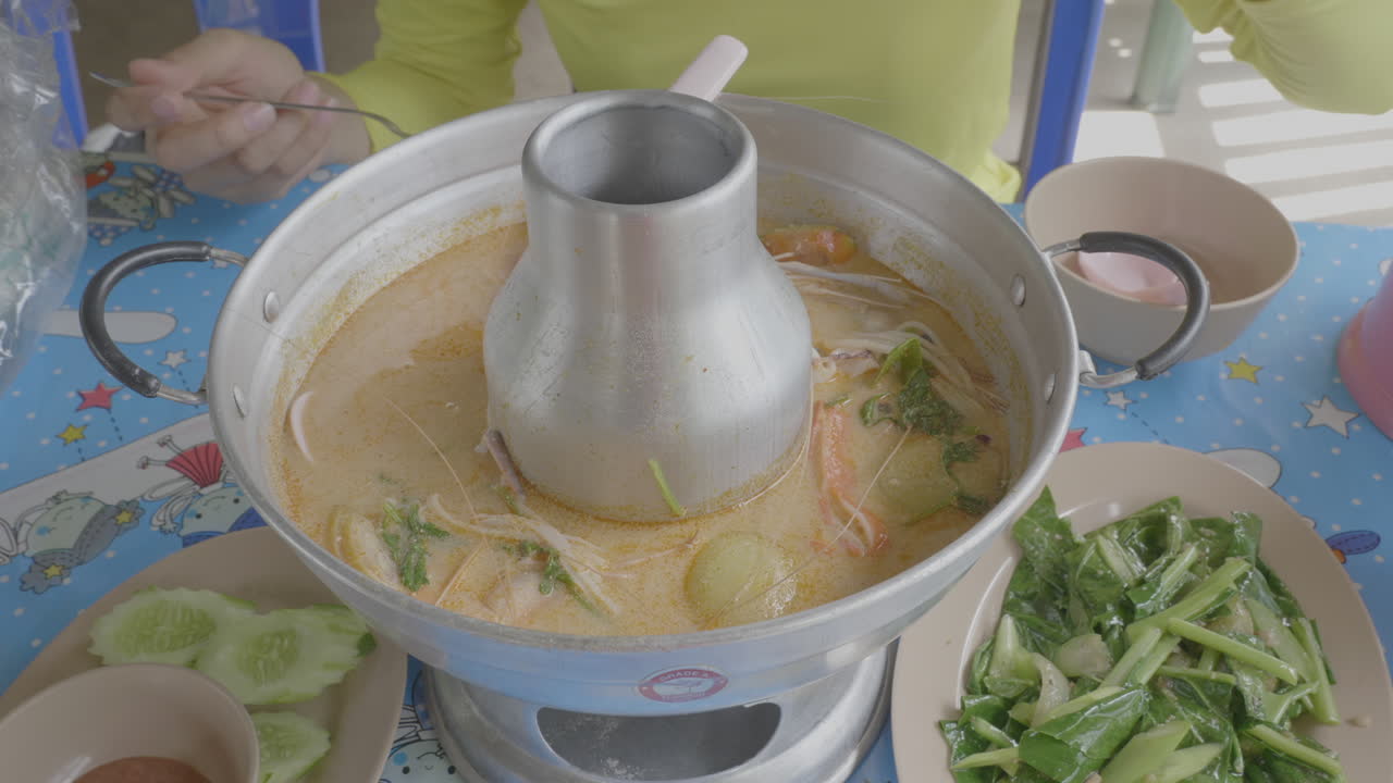 숯불 냄비에 담긴 동남아 그린 카레를 숟가락으로 떠서 먹다