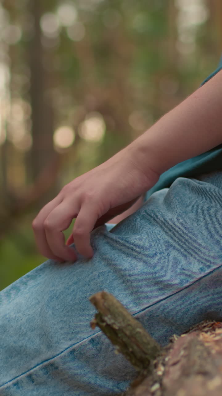 vista lateral de un excursionista descansando en un árbol caído con una bolsa roja y una tela drapeada sobre él en un entorno pacífico de bosque, vestido casualmente con vaqueros, la mano descansando en la pierna
