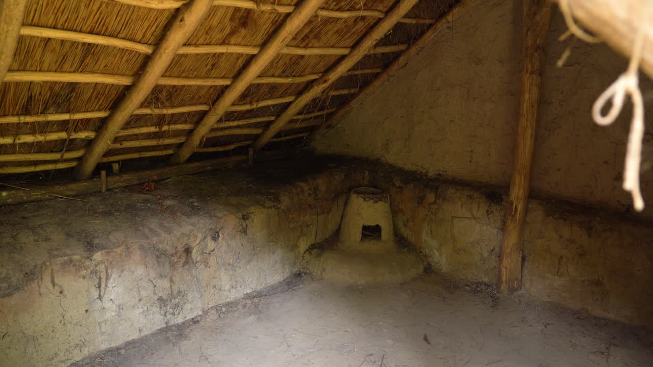 Clay oven built into corner of simple earthen hut with thatched roof over