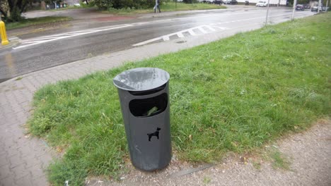 a following shot of a dog waste trash can with a dog amblem on it while it rains