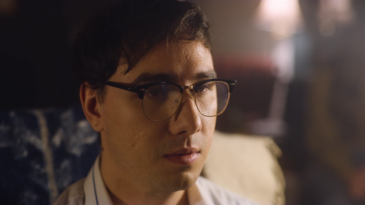 Man sits uncomfortably at party, he sweats and smokes.