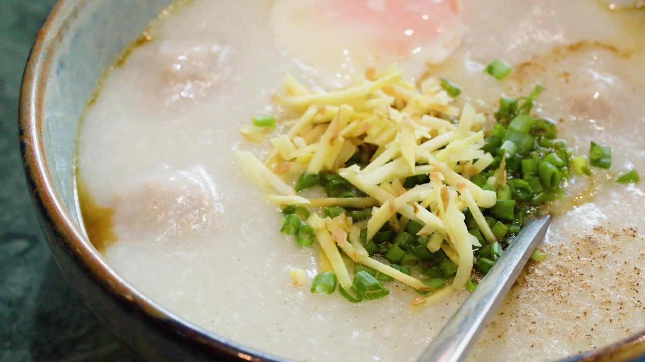 Tampilan dekat bubur nasi Thailand dengan abon babi, jahe, dan telur dalam mangkuk keramik