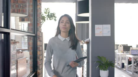 Mujer-De-Negocios-Casual-Birracial-Caminando-Por-La-Oficina-Con-Tableta,-Cámara-Lenta