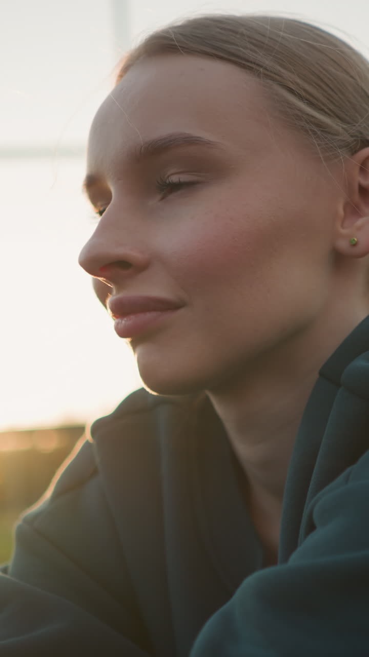 joven con capucha verde involucrada en actividades deportivas al aire libre, la luz del sol creando un resplandor dorado alrededor de sus hombros con campo abierto y valla en el fondo durante la hora de oro