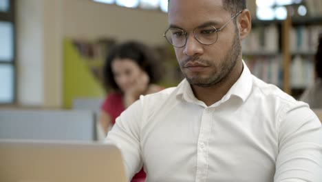 focused young man using laptop at library