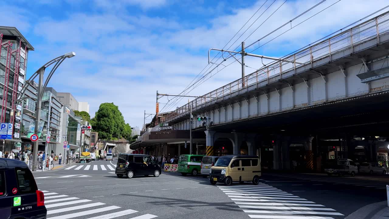 Busy city intersection under a railway bridge with cars and people on a sunny day