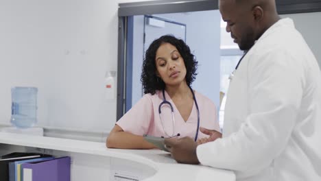 busy diverse doctors using tablet and talking in hospital in slow motion