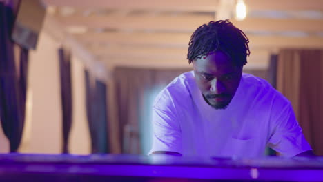 focused man working behind bar counter in modern lounge with purple lighting. he is preparing for an evening shift, adjusting equipment in a well-lit, stylish professional environment