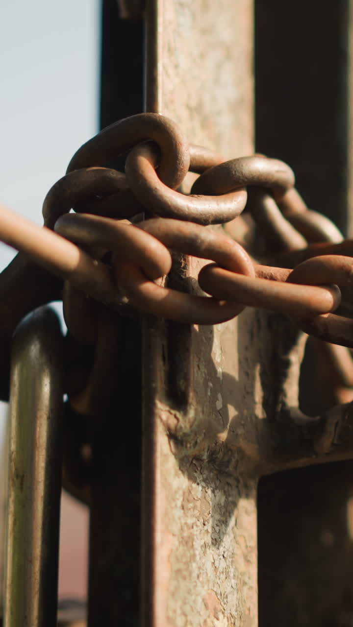 Closeup rusted chain on gate, corroded padlock and weathered metal post bathed in warm sunlight, flaking patina and gritty rust texture, shallow depth of field, abandoned urban scene suggesting