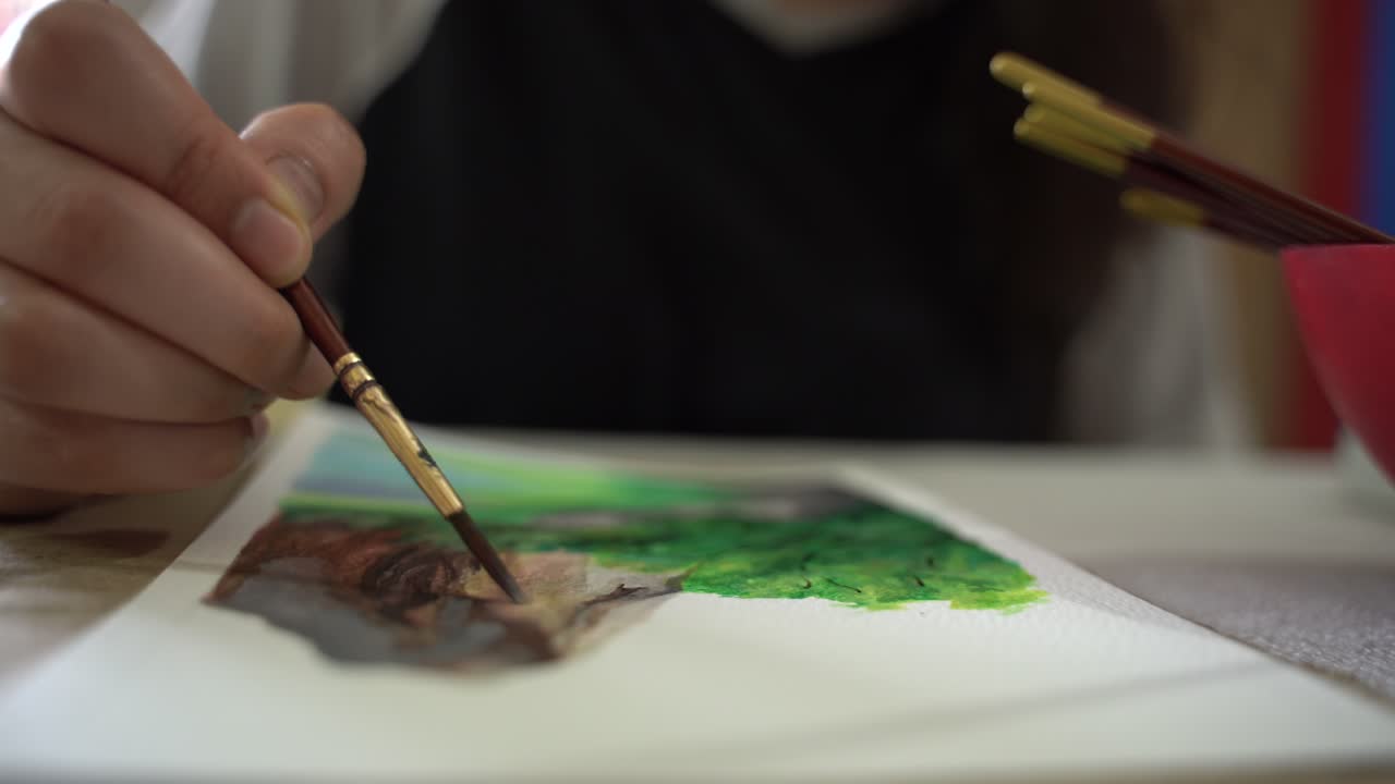 gran angular de un primer plano extremo de un artista dibujando un paisaje montañoso en papel de su imaginación usando colores de pintura gouache