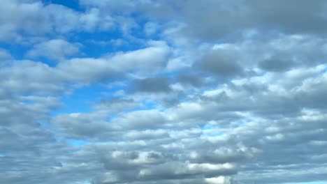 white cumulus clouds moving harmoniously casting lights and shadows over a blue sky background