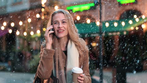 vista de cerca de una mujer caucásica hablando por teléfono inteligente en la calle mientras nieva en navidad