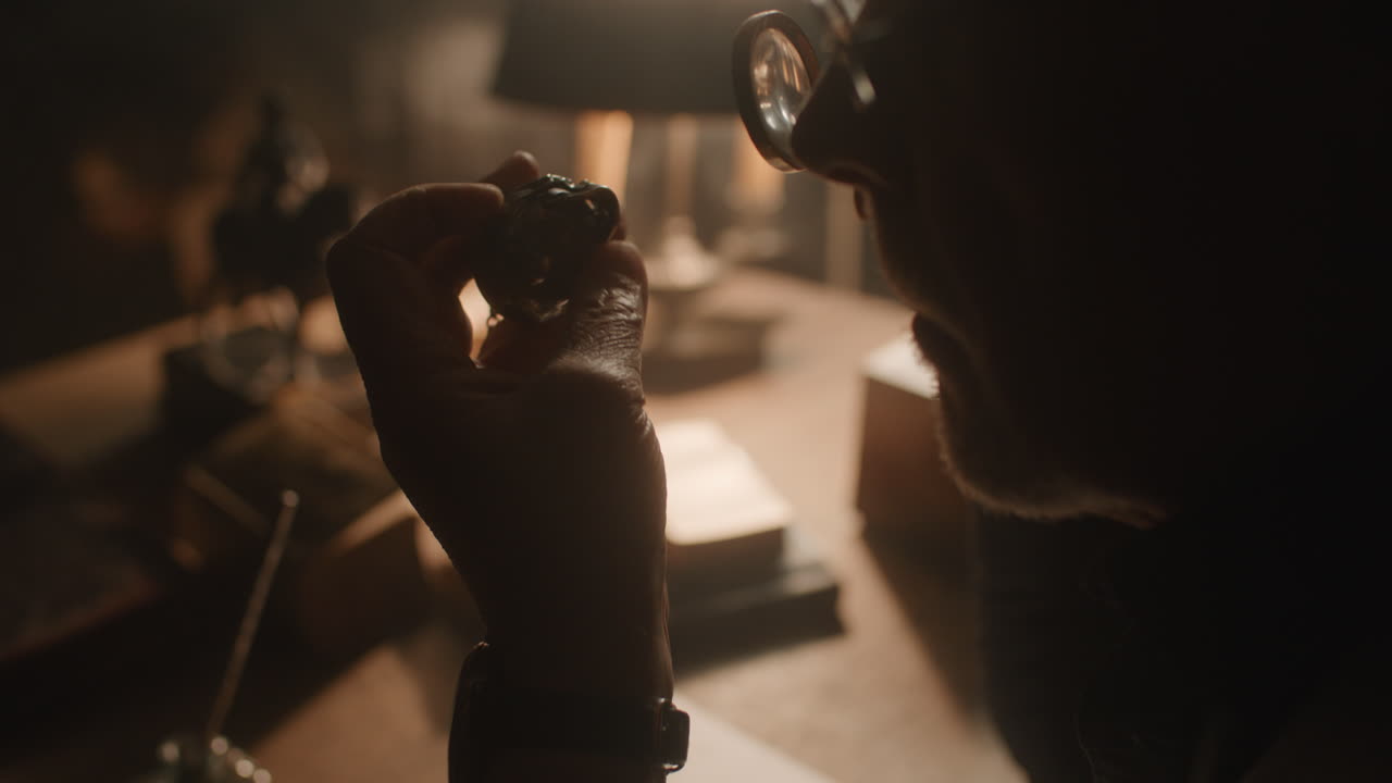 Older passionate man evaluates an old silver skull watch in his office at night
