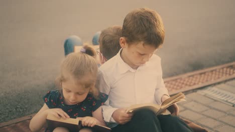 serious-children-read-textbooks-sitting-on-grey-pavement