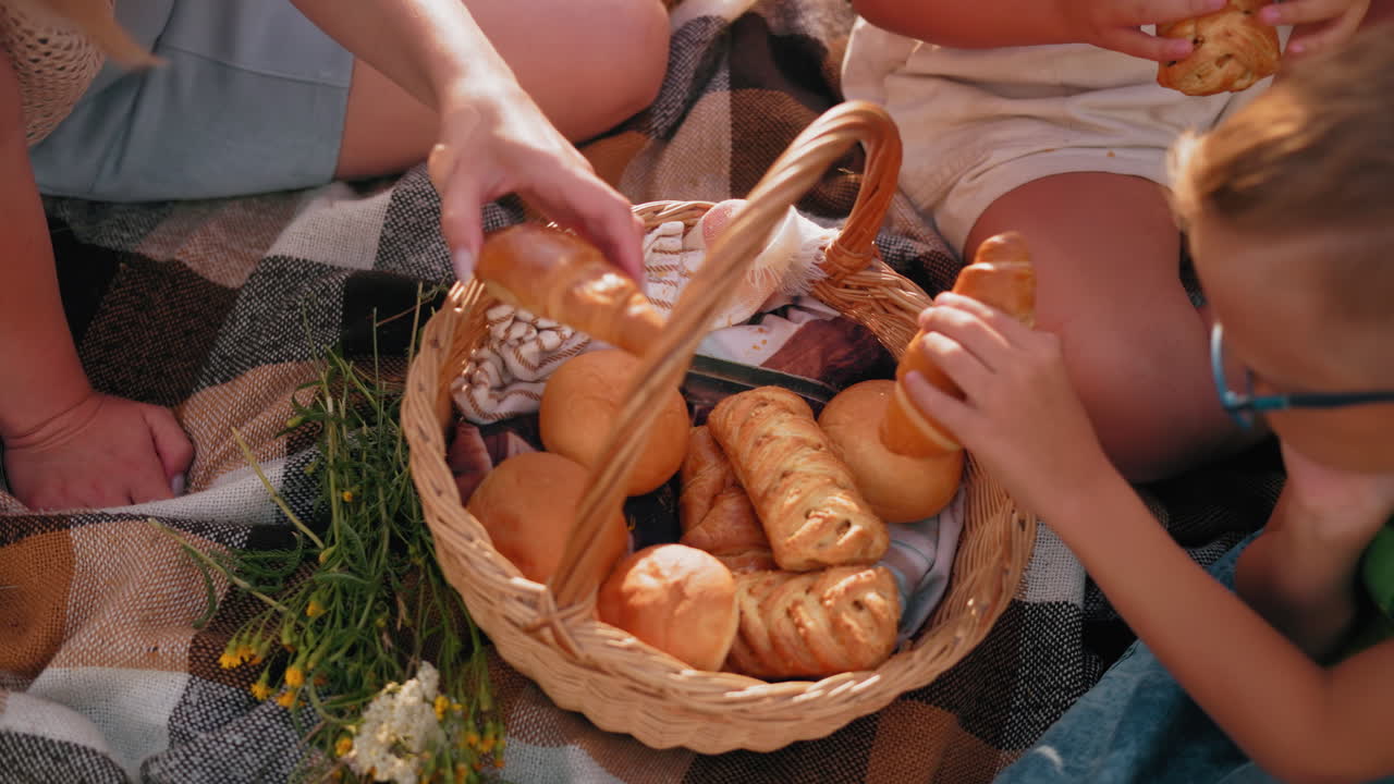 신선하게 구운 간식으로 가득 찬 피크닉 바구니에 손을 는 클로즈업, 붕대 손으로 페이스트리를 선택하는 사람, 다른 사람들이 체크 된 담요에 앉아있는 동안