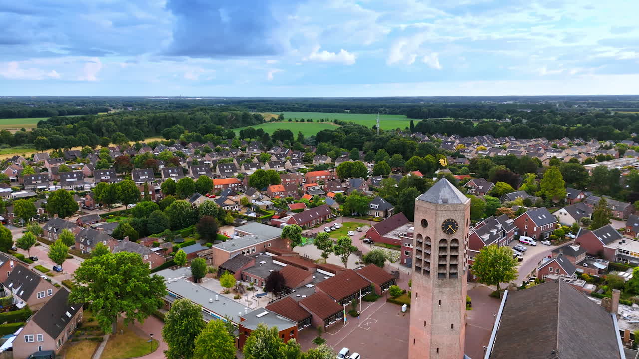 Overview of a serene village in summer. A picturesque village features lush greenery, quaint houses, and a prominent clock tower under a cloudy sky