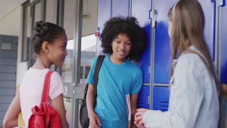 video of three diverse, happy schoolgirls talking by lockers in school corridor, copy space
