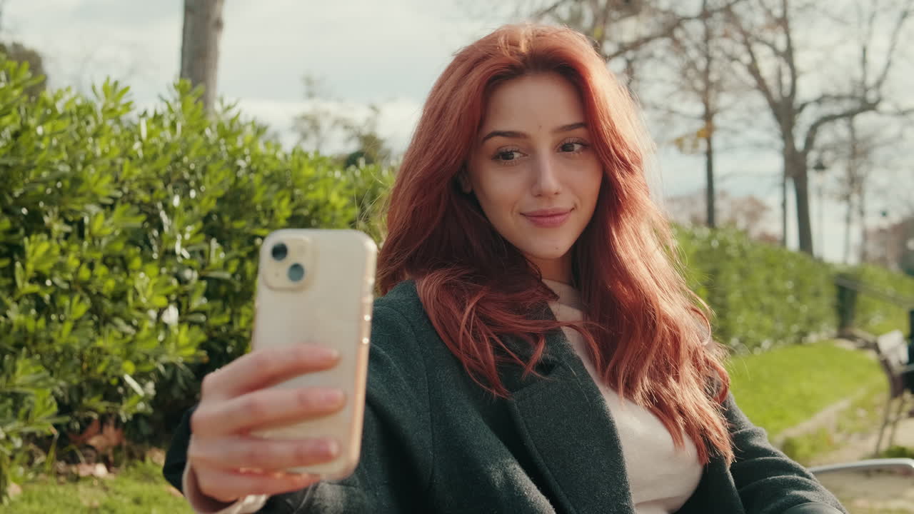 Giovane donna rossa che si scatta un selfie con lo smartphone al parco