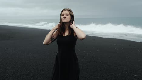 young beautiful woman in black dress dancing on black sand beach iceland, slow motion walking, dramatic waves seascape