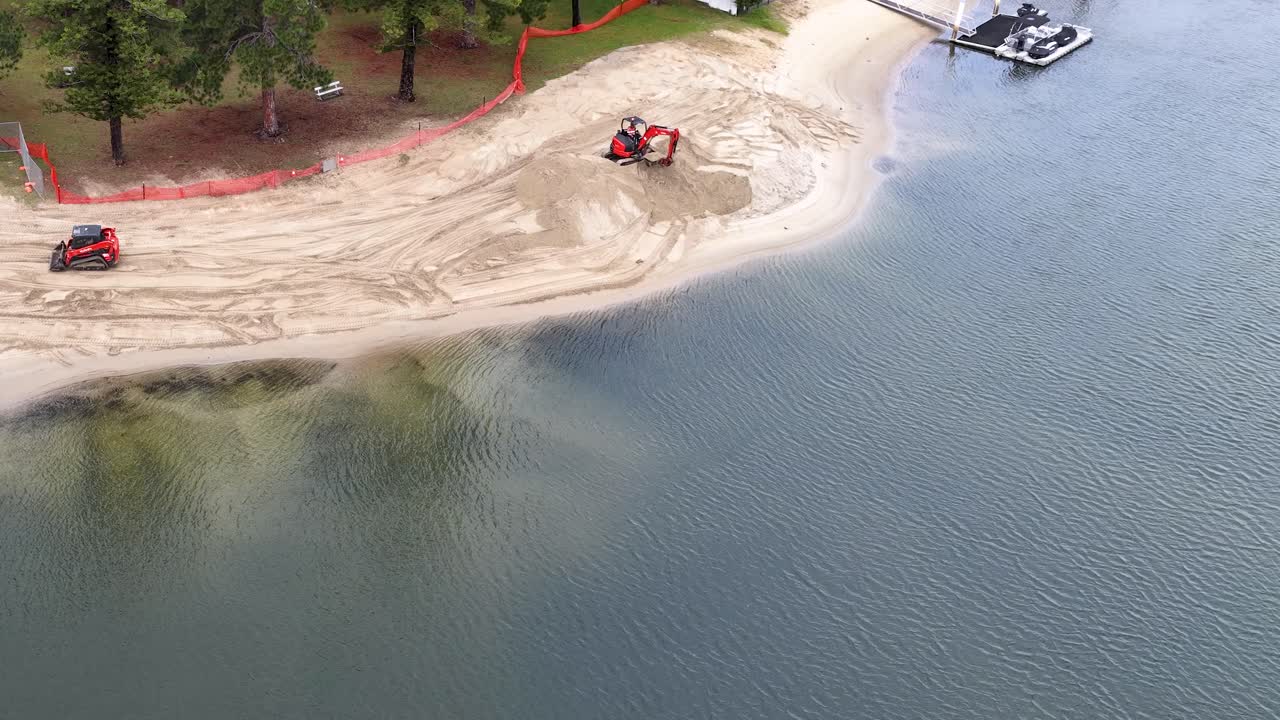 Ripresa aerea dall'alto di macchinari pesanti che eseguono il ripristino della sabbia su una spiaggia di un canale costiero.