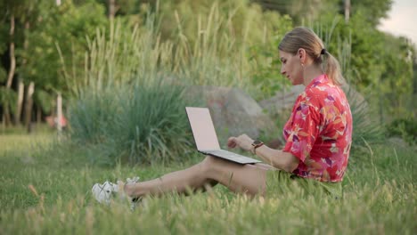 a middle-aged woman works using her laptop in a public park. she types and thinks.