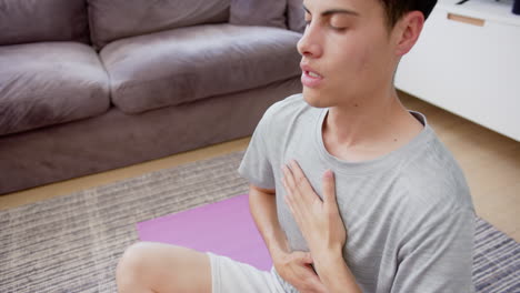 biracial man practicing yoga meditation sitting on living room floor, copy space, slow motion