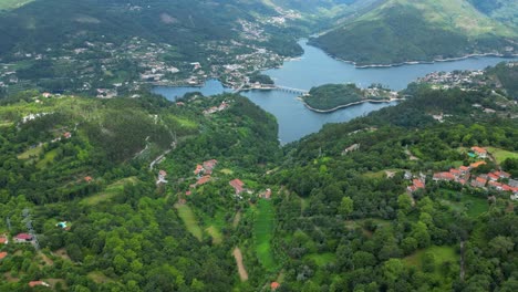 Vista-Aérea-De-Casas-En-El-Parque-Nacional-Peneda-Gerês,-Portugal,-Con-La-Presa-De-Caniçada-En-El-Fondo-Del-Día-Soleado