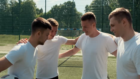 happy street football team putting hands together in huddle on the pitch before game