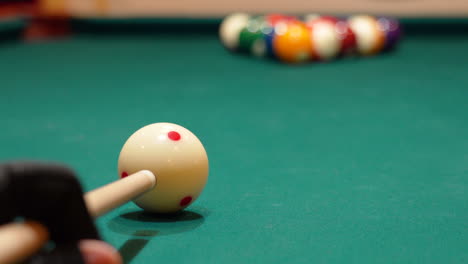 low angle closeup of cue ball as person wearing glove breaks rack of 8 ball powerfully on a pool table with green felt and the cue stick bending as both solid and stripe balls scatter, no faces in bar