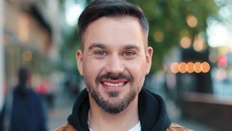 close-up view of caucasian bearded man using smartphone in the street and smiling at camera